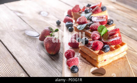 Cialde viennese con confettura di fragole, fresche fragole, lamponi mirtilli e scaglie di cioccolato su un tavolo di legno. La deliziosa prima colazione concept Foto Stock