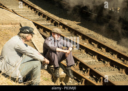 Chiusura del Regno Unito treno a vapore equipaggio (driver & fireman) fuori della locomotiva vintage, seduto sul binario ferroviario in sole splendente, in attesa del segnale per andare. Foto Stock