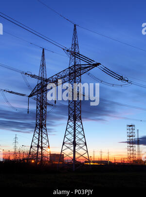 La trasmissione di energia elettrica pilone stagliano contro il cielo blu al tramonto Foto Stock