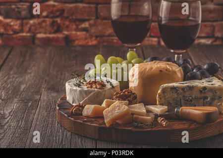 Formaggio, noci, uva e vino rosso su sfondo di legno, fuoco selettivo. Foto Stock