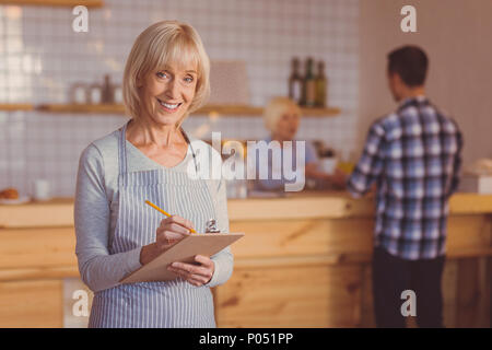 Sorridente cameriere anziani controllo elenco degli ordini Foto Stock