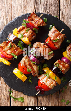 Preparato di fresco gli spiedini di carne di maiale con verdure close-up su una piastra di ardesia su un tavolo. Verticale in alto vista da sopra Foto Stock