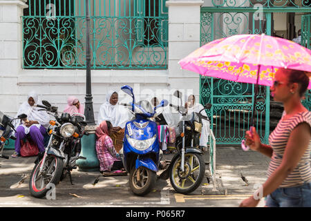 Una giovane donna camminare davanti a un gruppo di donne sedute sulla strada in attesa di alms al di fuori della moschea Jummah un venerdì, Port Louis, Maurizio Foto Stock