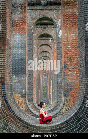 Donna seduta negli archi del Ouse Valley viadotto a praticare yoga e meditazione Foto Stock