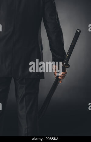 Ritagliato colpo di uomo in business suit con spada katana su nero Foto Stock