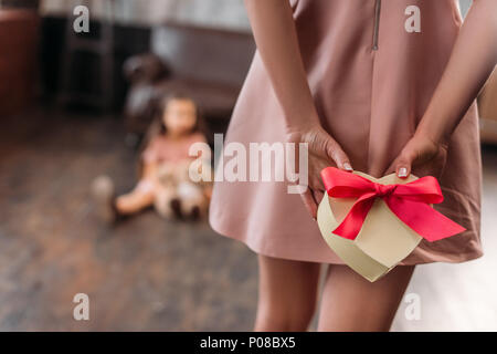 Ritagliato colpo di madre nascondendo regalo di compleanno per la figlia di dietro la schiena Foto Stock