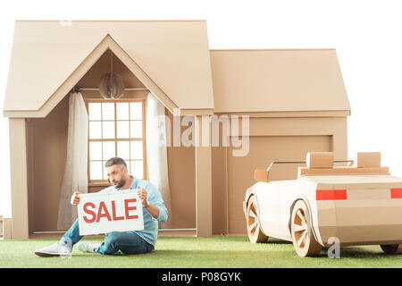 Uomo con vendita cartello davanti casa di cartone isolato su bianco Foto Stock