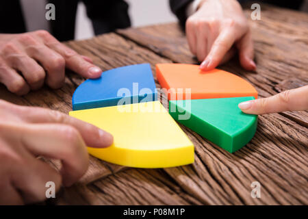 Gli imprenditori pezzi di collegamento di multi colore grafico a torta sulla scrivania in legno Foto Stock