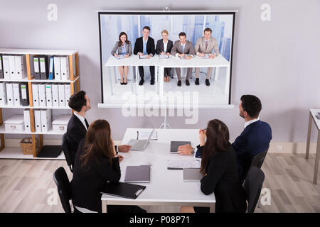 Gruppo di imprenditori alla ricerca di un proiettore con il laptop sulla scrivania in ufficio Foto Stock