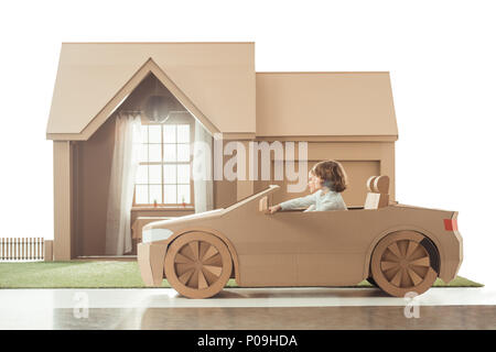 Vista laterale di equitazione per bambini auto di cartone davanti la casa isolata su bianco Foto Stock