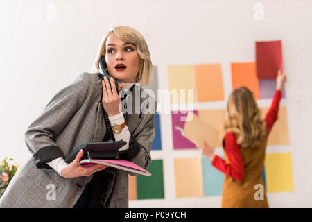 Magazine editor parlando al telefono mentre il suo collega di lavoro con la tavolozza di colori dietro Foto Stock