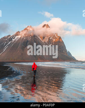 L'uomo, turistici passeggiate sulla spiaggia di sabbia nera, spiaggia di lava, riflessione, montagne Klifatindur, Eystrahorn e Kambhorn Foto Stock