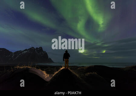 Night Shot, uomo guarda la Northern Lights (Aurora boreale), la spiaggia di sabbia nera, montagne Klifatindur, Eystrahorn e Kambhorn Foto Stock