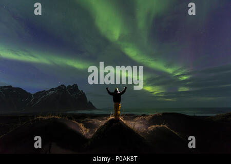 Night Shot, uomo guarda la Northern Lights (Aurora boreale), la spiaggia di sabbia nera, montagne Klifatindur, Eystrahorn e Kambhorn Foto Stock