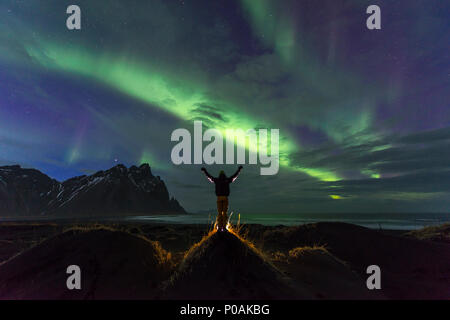 Night Shot, uomo guarda la Northern Lights (Aurora boreale), la spiaggia di sabbia nera, montagne Klifatindur, Eystrahorn e Kambhorn Foto Stock