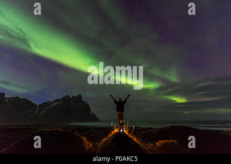 Night Shot, uomo guarda la Northern Lights (Aurora boreale), la spiaggia di sabbia nera, montagne Klifatindur, Eystrahorn e Kambhorn Foto Stock