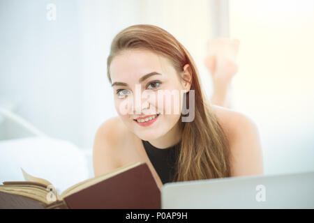 Bella donna la lettura di un libro e sorriso giacciono sul letto Foto Stock