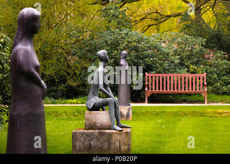 Tre statue in un parco di fronte a un banco vuoto Foto Stock