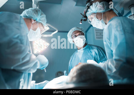 Vista dal basso dei chirurghi multiculturale operando il paziente in sala operatoria Foto Stock