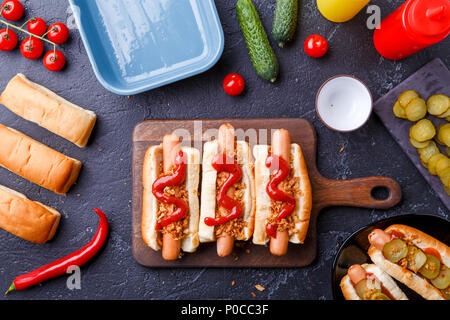 Foto sulla parte superiore di panini con salsicce sul tagliere, su tavola con cetrioli Foto Stock