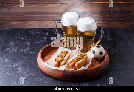 Foto di due bicchieri di birra e hot dogs sul vassoio in legno con il calcio Foto Stock
