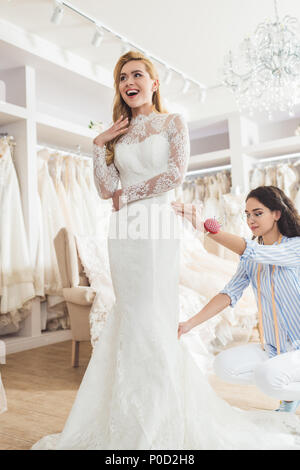 Bionda sposa abito in pizzo e adattare durante il montaggio del vestito in un salone per matrimoni Foto Stock