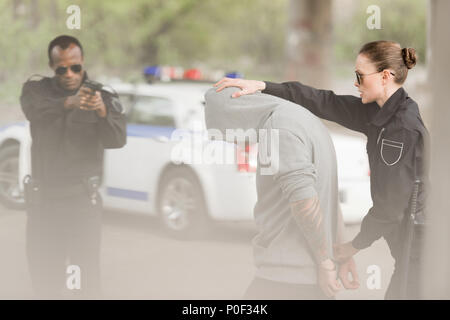 Poliziotta holding criminale poliziotto mentre la pistola di puntamento a lui Foto Stock