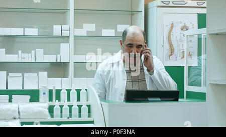 Il farmacista di parlare con il cliente tramite telefono cellulare in farmacia Foto Stock