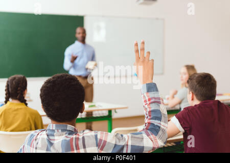 Vista posteriore di African American Boy con braccio fino in aula con docente e compagni di classe Foto Stock