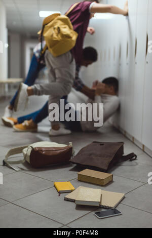 Inquadratura sfocata di scolaro essendo intimorito dai compagni di scuola in corridoio sotto gli armadietti con fuoriuscite di libri da zaino sul pavimento Foto Stock