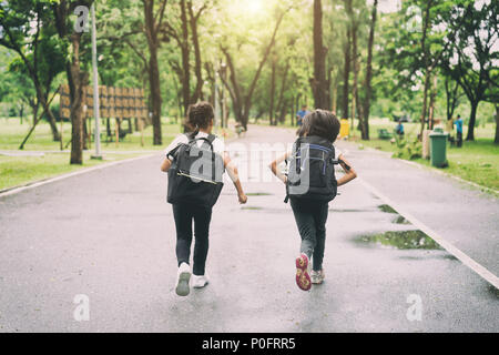 Due alunni della scuola primaria eseguire vai a scolastici. Due ragazza con sacchi dietro la schiena. Calda giornata di caduta. Si torna a scuola. Poco prima livellatrici. Foto Stock