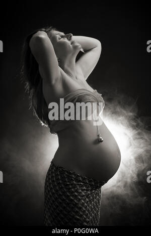 Studio ritratto di donna incinta, Jingle Bell in appoggio sulla pancia, testa indietro, toccando i capelli, in bianco e nero Foto Stock