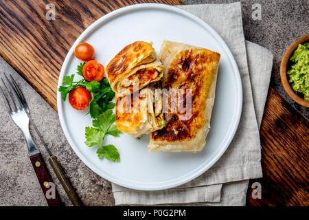 Chimichanga messicano sulla piastra bianca servito con salsa guacamole. Fried tortilla farcita con pollo e verdure. Tradizionale cibo messicano, vista dall'alto Foto Stock