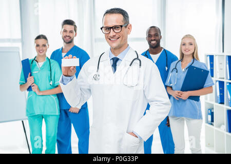 Bella coppia medico della scatola di contenimento di pillole con i colleghi in piedi insieme sullo sfondo Foto Stock