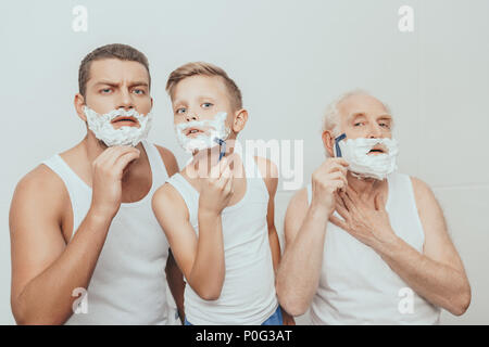 Padre e Figlio e nonno in piedi con la crema di rasatura sui loro volti la rasatura con il rasoio, isolato su bianco Foto Stock