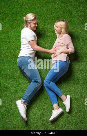 Al di sopra di vista della giovane donna incinta con il suo fidanzato giacente insieme sull'erba Foto Stock