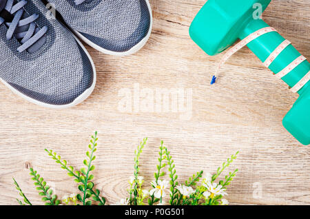 Piatto sport laici composizione con il grigio sneakers, manubri e fiore su sfondo di legno. Concetto di uno stile di vita sano, lo sport e la dieta. Vista dall'alto. Foto Stock