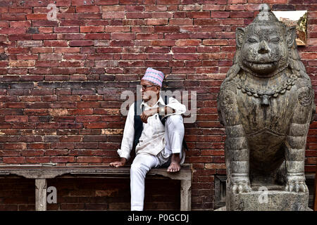 Un anziano nepalese seduto accanto ad una statua a Kathmandu, Nepal Foto Stock