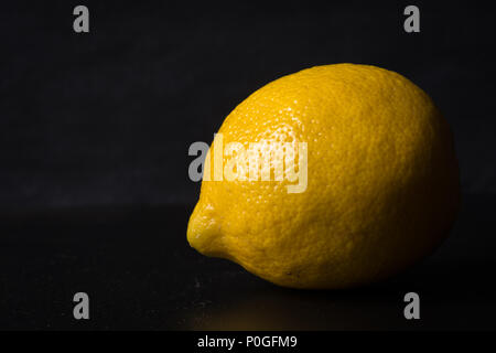 Limone isolato su sfondo scuro illuminato laterale che mostra la texture. Foto Stock