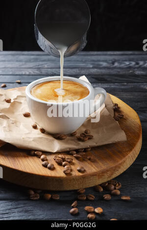 Versare la crema per tazza di caffè. Un flusso di latte si versa nel bicchiere. Foto Stock