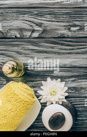 Lay piatto con spa e trattamenti di massaggio disposizione con asciugamano, olio essenziale, ciottoli e crisantemo fiore su sfondo di legno Foto Stock