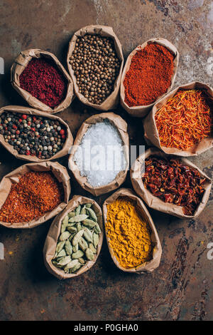 Vista dall'alto di coriandolo, zafferano e scaglie di peperoncino in sacchi di carta sul tavolo Foto Stock