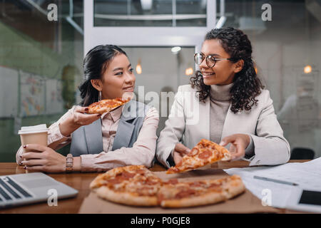 Multietnica imprenditrici a pranzo in ufficio, mangiare la pizza Foto Stock