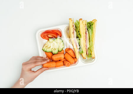 Immagine ritagliata della donna prendendo la carota dalla scatola di pranzo isolato su bianco Foto Stock