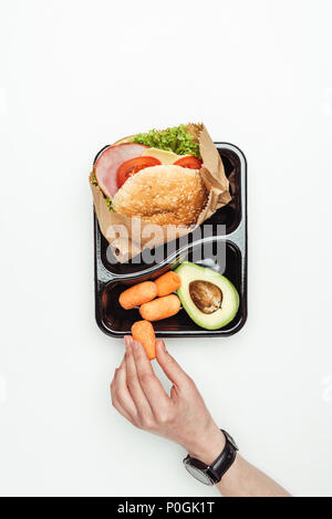 Immagine ritagliata della donna prendendo la carota dal contenitore da asporto isolato su bianco Foto Stock