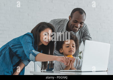 African American madre puntando su qualcosa al portatile a casa Foto Stock