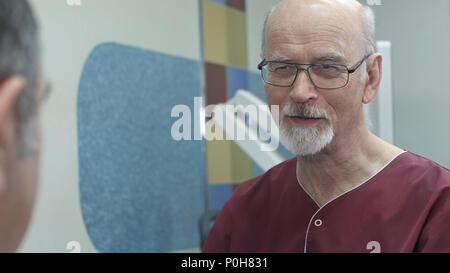 Positivo medico senior discutendo con i senior uomo in ospedale Foto Stock