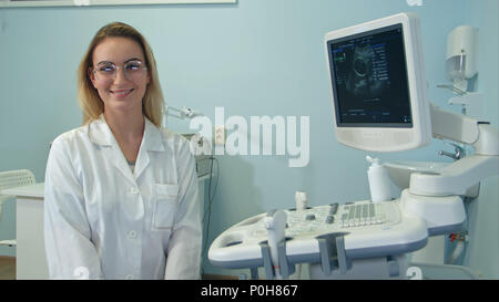 Donna sorridente medico in bicchieri cercando la fotocamera nella camera ad ultrasuoni Foto Stock
