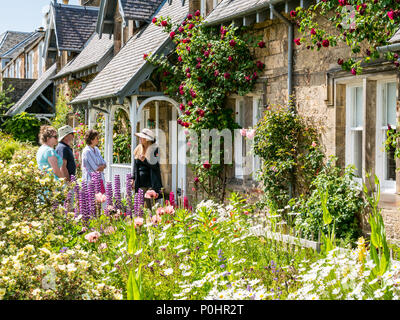 Dirleton Village Gardens, Scotland’s Gardens Scheme 2018, 9 giugno 2018. Dirleton Village, East Lothian, Scozia, Regno Unito. I residenti del villaggio aprono i loro giardini al pubblico come parte del programma giardini nazionali. Cottage pittoreschi. I visitatori che ammirano il giardino in una giornata di sole parlano con il proprietario che indossa un cappello di paglia Foto Stock