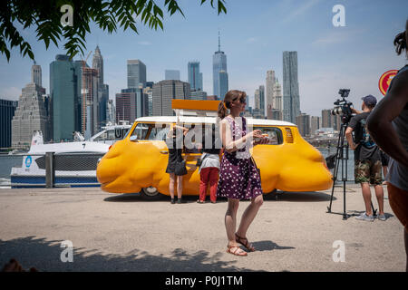 Brooklyn, Stati Uniti d'America. Il 9 giugno 2018. Con lo skyline di New York dietro di loro i visitatori al Ponte di Brooklyn Park di New York delizia in artista Erwin Wurm 'Hot Dog Bus' che serve libera hot dogs a qualsiasi e tutti, visto in apertura di giornata, sabato 9 giugno, 2018. L'artista austriaco modificato un vintage Microbus Volkswagen in un bulbo di colore giallo brillante cibo carrello, ridefinendo la dicotomia tra il commercio e la scultura, pur servendo iconica libero New York street food. Il carrello è stato precedentemente il "Curry Bus' che serve wursts in Europa. Credito: Richard Levine/Alamy Live News Foto Stock